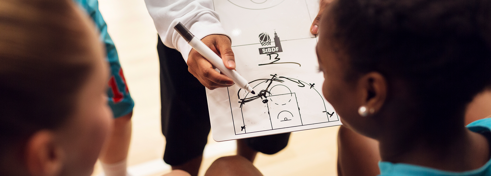 Någon visar en teckning med spelstrategi för två baskettjejer. 