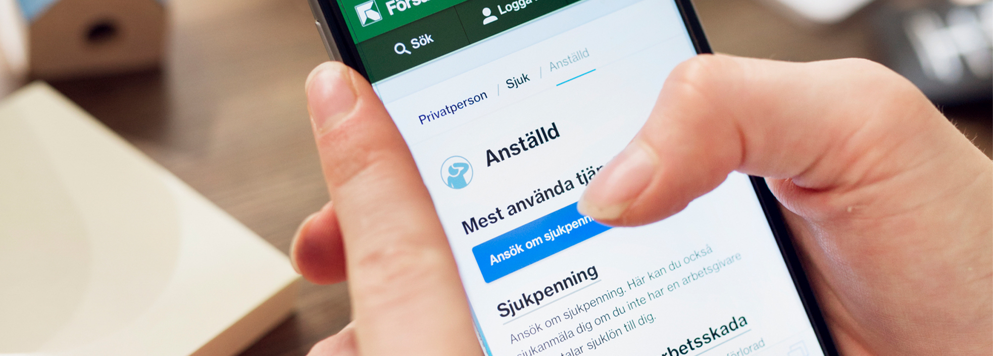 Någon håller i en mobiltelefon. På skärmen visas en samhällstjänst för sjukanmälningar. 