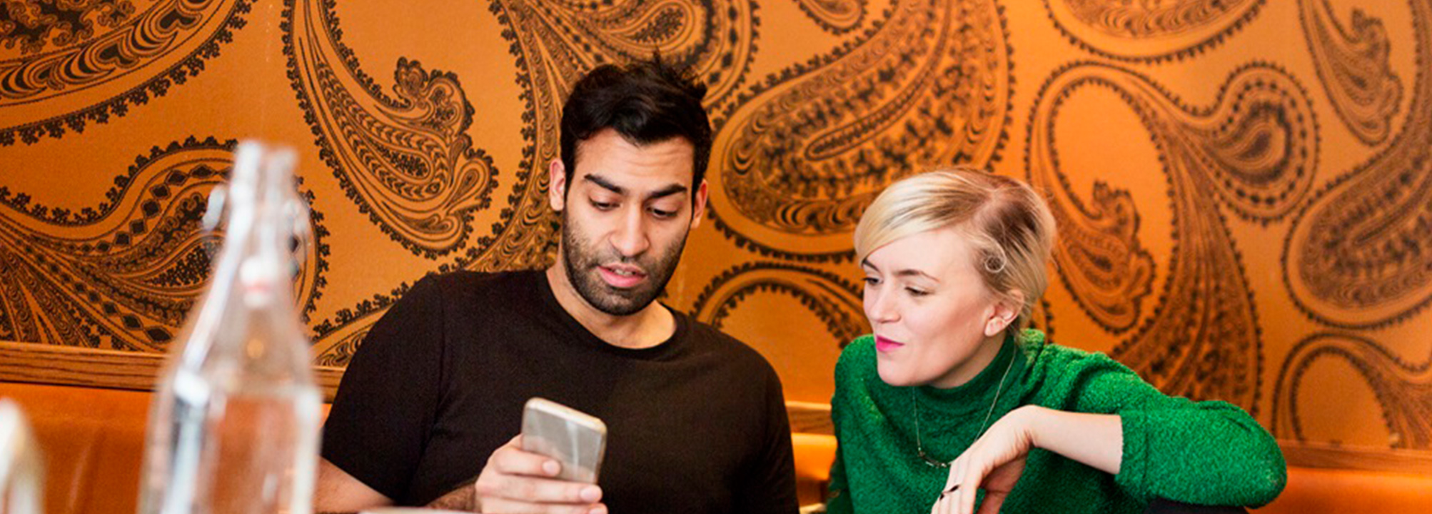 Två personer sitter på ett café och tittar på mobil