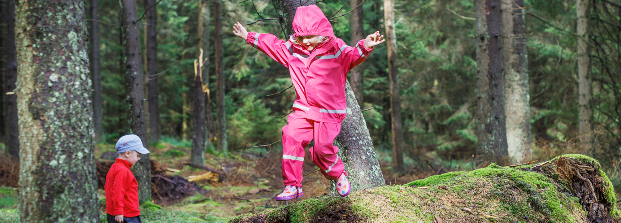 Barn hoppar från sten i skog.