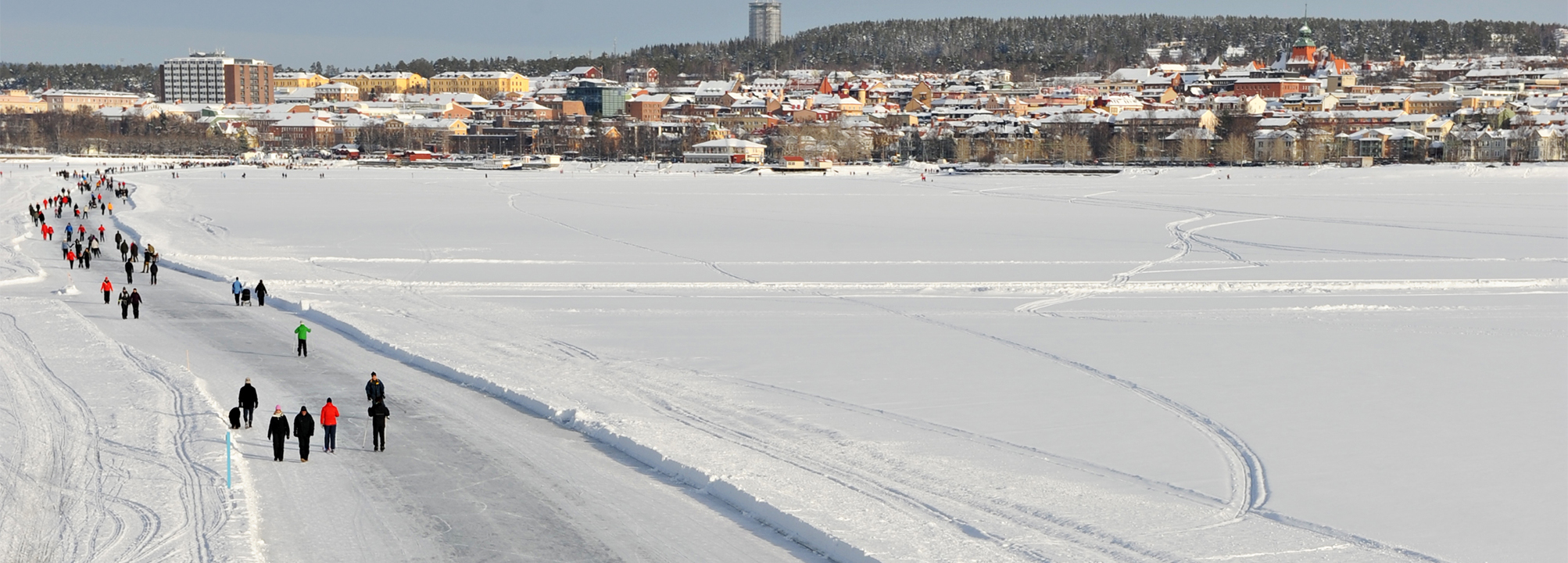 Människor som promenerar på en plogad bana på en snötäckt sjö.