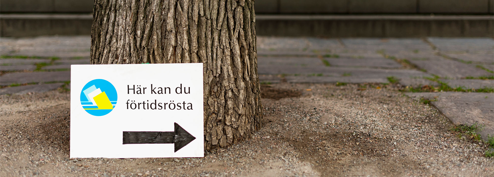 En skylt lutad mot ett träd pekar mot en lokal för förtidsröstning