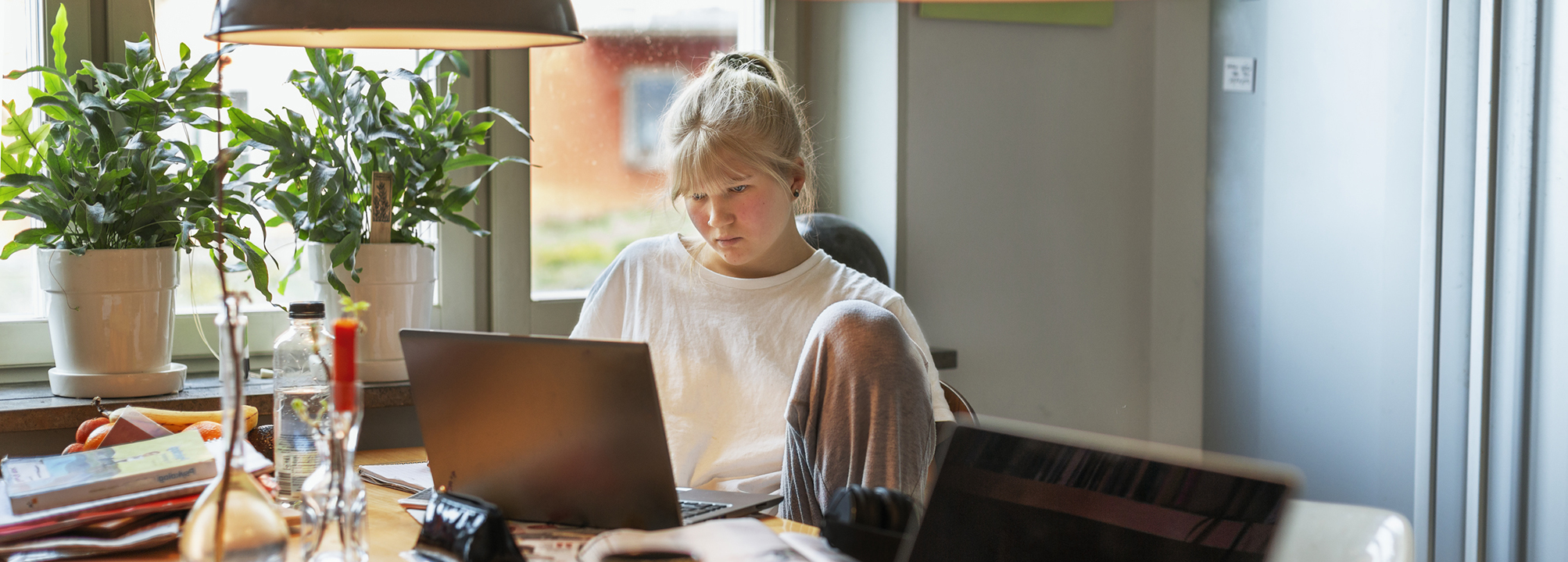 En tjej sitter framför en laptop vid köksbordet