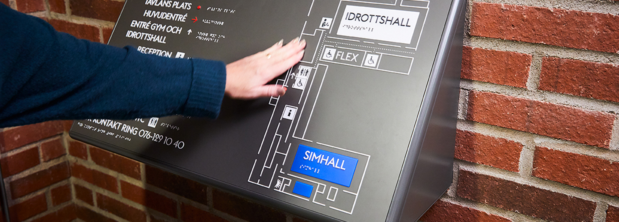 En person läser informationstavla på punkt i idrottshall.