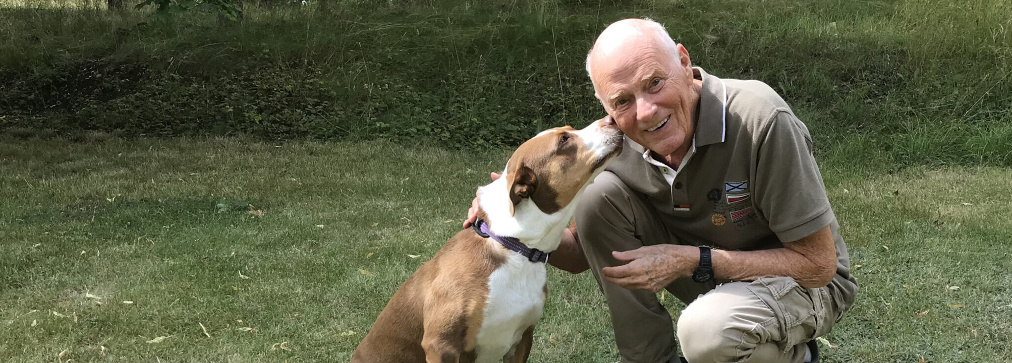 Anders Hallgren sitter på huk på en gräsmatta med en brun hund.
