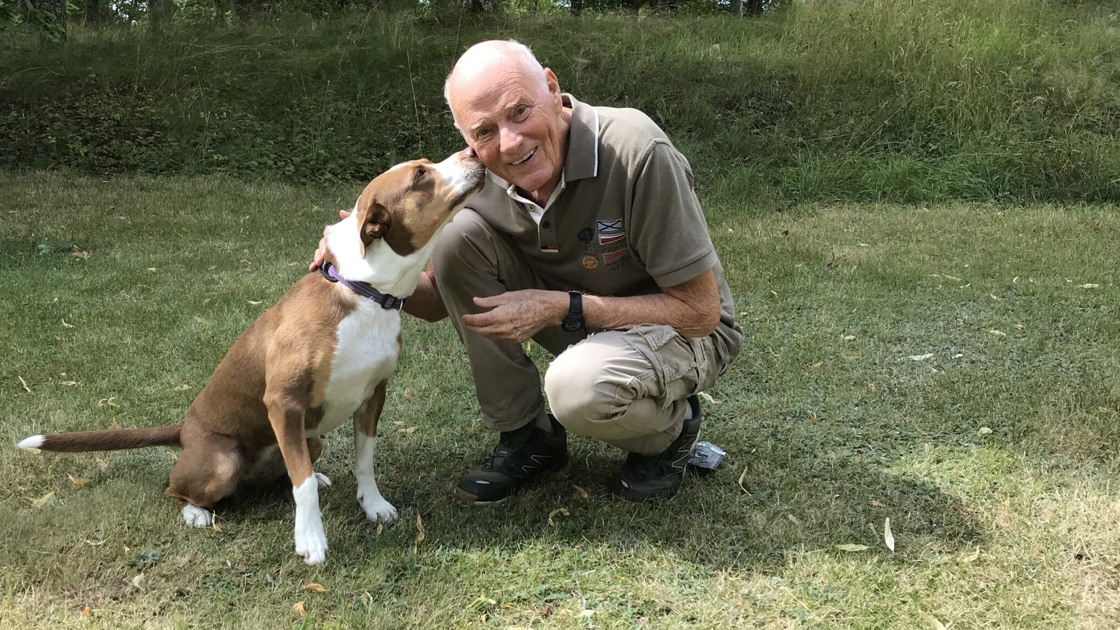 Anders Hallgren sitter på huk på en gräsmatta med en brun hund.