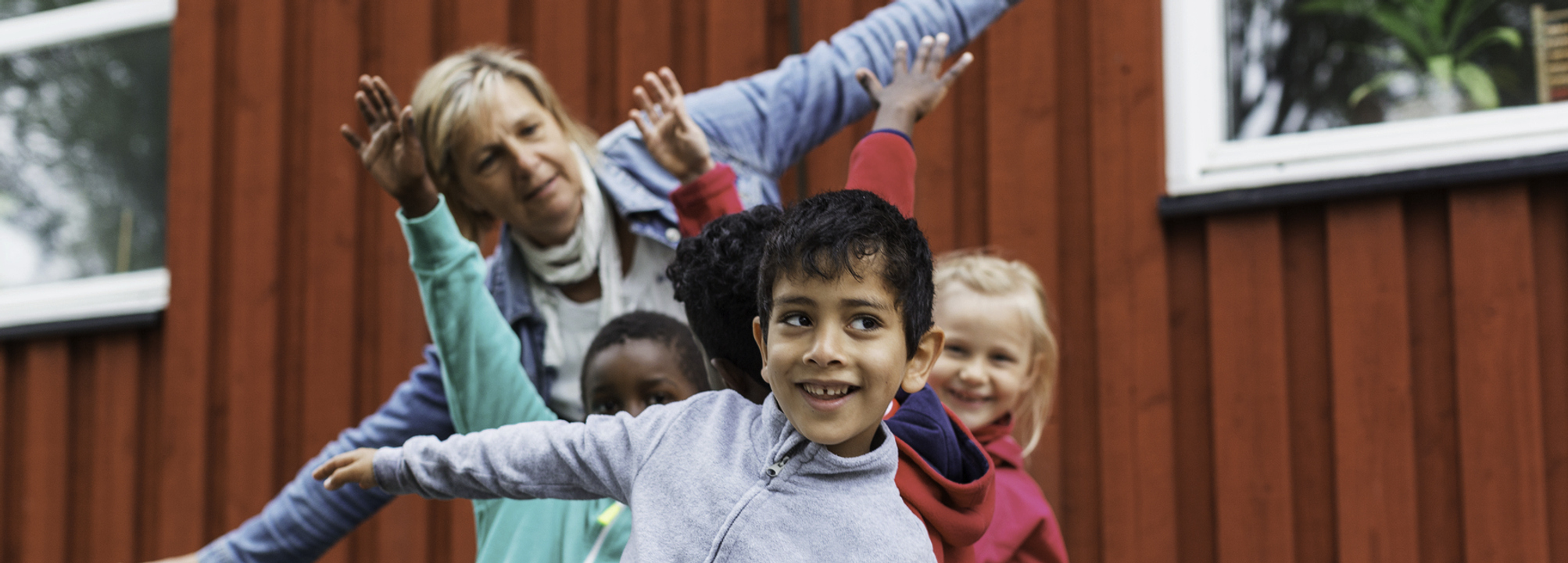 Tre barn och pedagog leker utomhus på förskola.