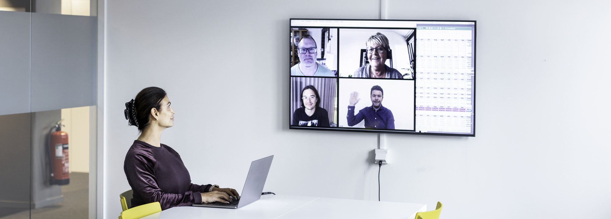 Kvinna i stort mötesrum har digitalt möte med kollegor.