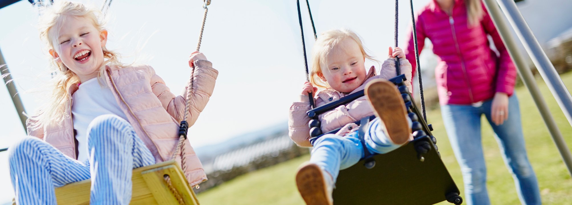 Två barn gungar i lekpark med sin mamma.