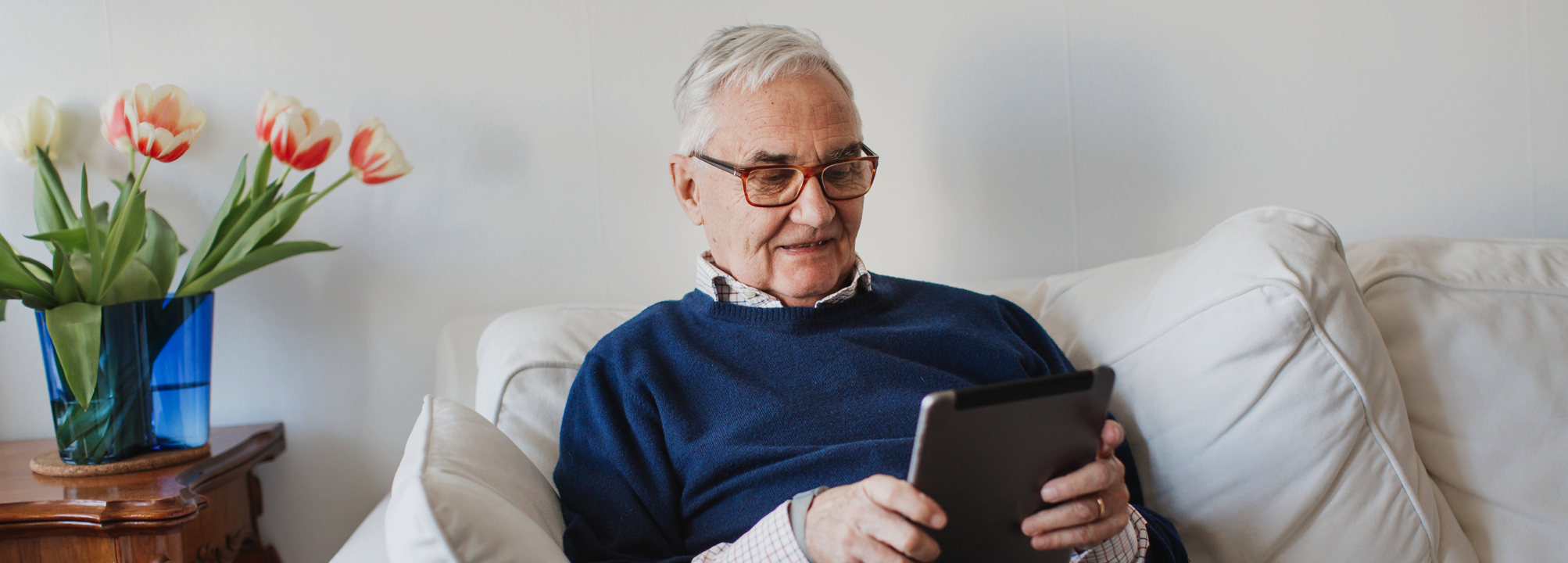 Äldre man i soffa sitter och klickar på sin surfplatta.