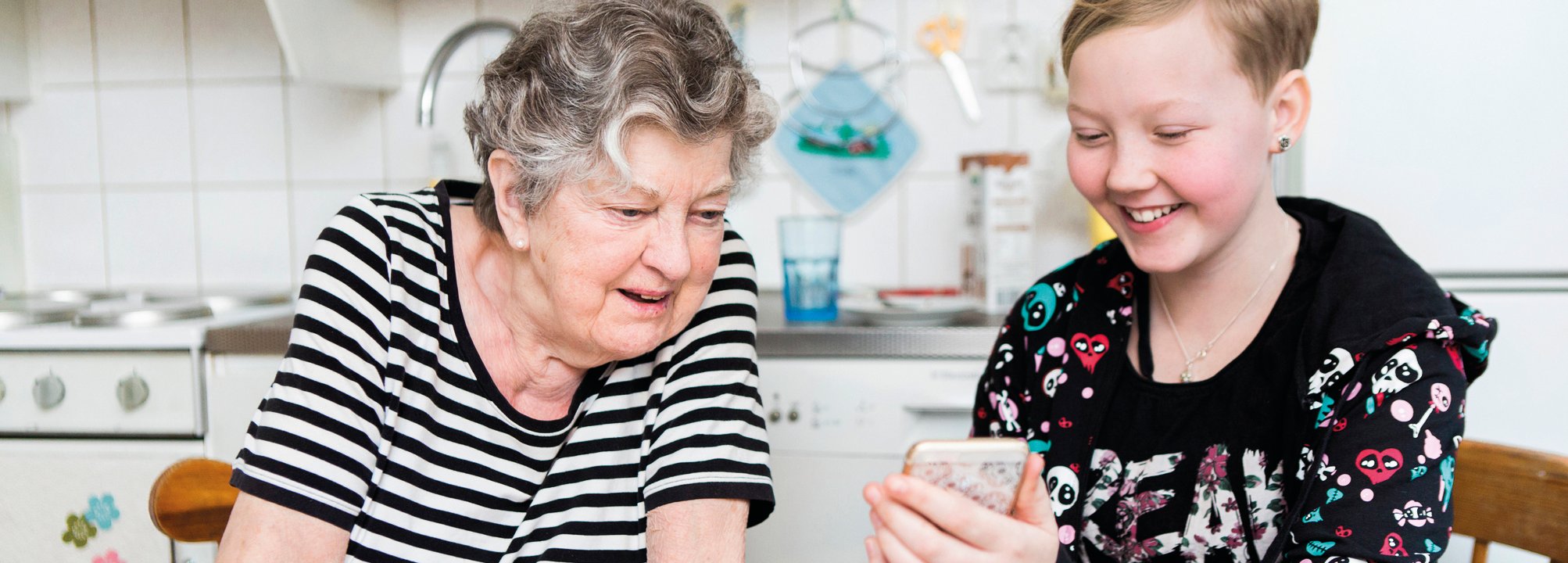 Flicka med äldre kvinna ler och tittar på mobiltelefon.