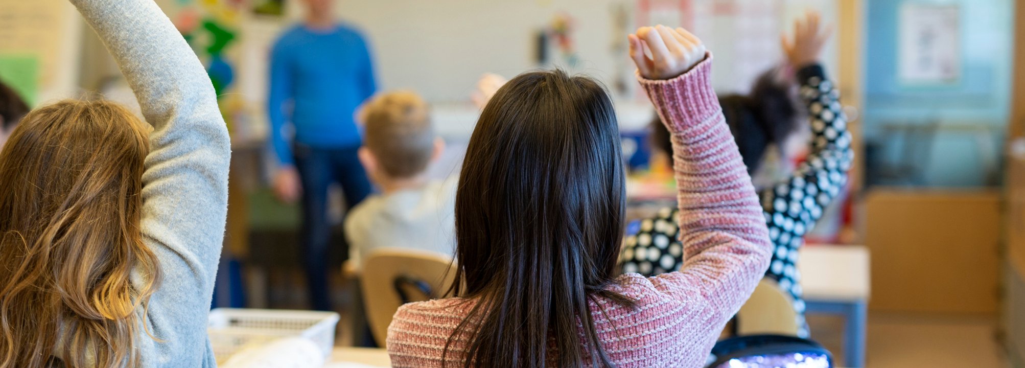En grupp barn som räcker upp händerna i ett klassrum.