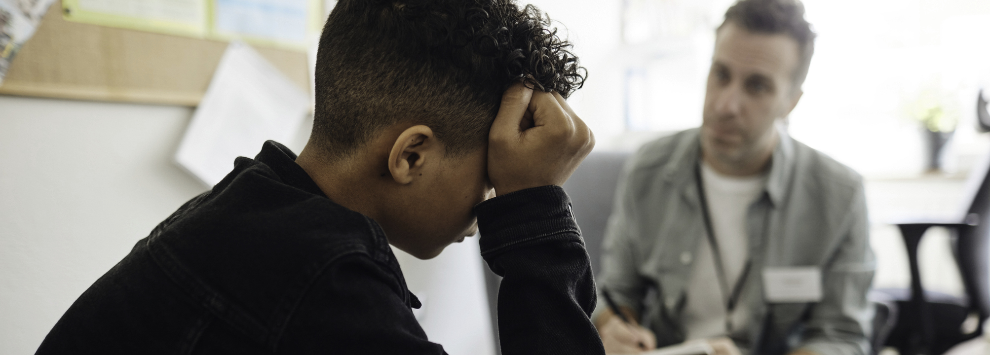 Nedstämd tonårspojke samtalar med vuxen skolpersonal.